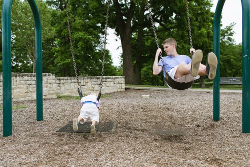 dad and son swinging on stomach at playground genuine moment