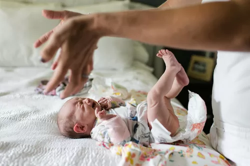 genuine documentary moment mom funny expresive hands during diaper change baby crying