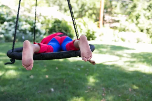 kid relaxing on swing in superman outfit real documentary photo