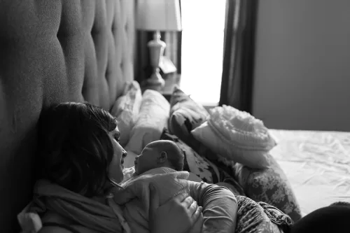 mom holding baby in bed in enduring sweet way in home session